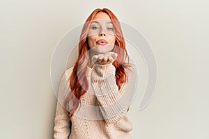 Young beautiful redhead woman wearing casual winter sweater looking at the camera blowing a kiss with hand on air being lovely and