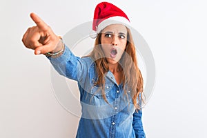 Young beautiful redhead woman wearing christmas hat over isolated background Pointing with finger surprised ahead, open mouth