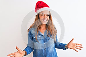 Young beautiful redhead woman wearing christmas hat over isolated background smiling cheerful with open arms as friendly welcome,