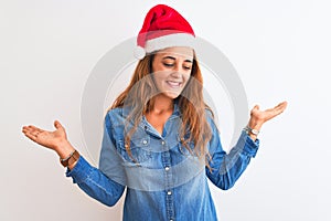 Young beautiful redhead woman wearing christmas hat over isolated background smiling showing both hands open palms, presenting and