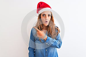 Young beautiful redhead woman wearing christmas hat over isolated background Surprised pointing with finger to the side, open