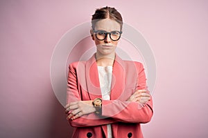 Young beautiful redhead woman wearing jacket and glasses over isolated pink background skeptic and nervous, disapproving