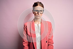 Young beautiful redhead woman wearing jacket and glasses over isolated pink background skeptic and nervous, frowning upset because
