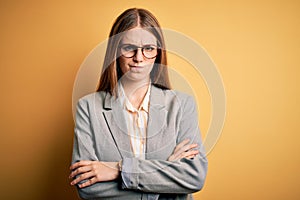 Young beautiful redhead woman wearing jacket and glasses over isolated yellow background skeptic and nervous, disapproving