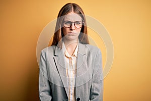 Young beautiful redhead woman wearing jacket and glasses over isolated yellow background skeptic and nervous, frowning upset