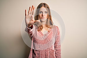 Young beautiful redhead woman wearing pink casual sweater over isolated white background doing stop sing with palm of the hand