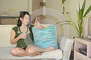 Young beautiful and relaxed Asian Chinese woman lying at home living room sofa couch using internet on mobile phone happy and comf