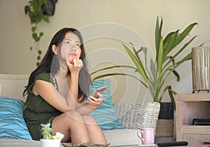 Young beautiful and relaxed Asian Chinese woman lying at home living room sofa couch using internet on mobile phone happy and comf