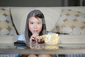 Young beautiful and relaxed Asian Chinese woman watching Korean drama on television on sad romantic movie eating popcorn at home