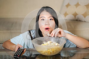 Young beautiful and relaxed Asian Japanese woman watching Korean drama on television on sad romantic movie eating popcorn at home