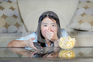 Young beautiful and relaxed Asian Japanese woman watching Korean drama on television on sad romantic movie eating popcorn at home