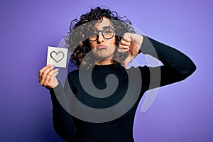 Young beautiful romantic arab woman wearing glasses holding reminder paper with heart with angry face, negative sign showing