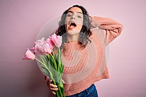 Young beautiful romantic woman with curly hair holding bouquet of pink tulips Crazy and scared with hands on head, afraid and