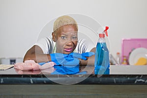 Young beautiful sad and depressed afro American black woman with detergent spray bottle working stressed and tired at home kitchen