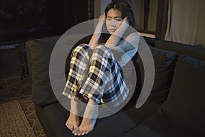 Young beautiful sad and depressed Asian Japanese woman in pain at living room sofa couch crying helpless and desperate suffering