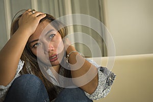 Young beautiful sad and depressed Asian woman in pain thoughtful and confused at home couch feeling broken heart suffering