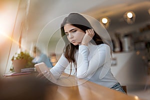 Young beautiful sad woman checking her smarphone looking upset while sitting in the cafe during lunch break, tough life concept