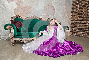 Young beautiful sad woman in fantasy rococo style medieval dress sitting on the floor near sofa