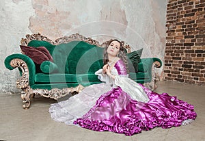 Young beautiful sad woman in fantasy rococo style medieval dress sitting on the floor near sofa