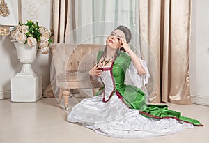 Young beautiful sad woman in green rococo style medieval dress sitting on the floor