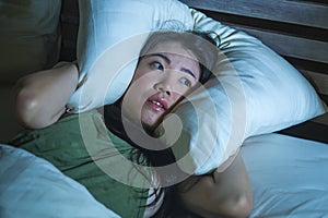 Young beautiful scared Asian Chinese woman lying awake in bed sleepless covering head with pillow suffering nightmare insomnia dis