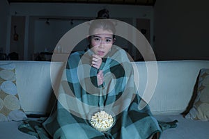 Young beautiful scared and frightened Asian Japanese woman watching horror scary movie or thriller eating popcorn in fear face