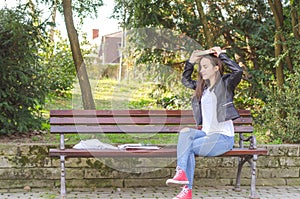 Young beautiful school or college girl with glasses sitting on the bench in the park reading the books and study for exam