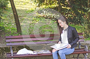 Young beautiful school or college girl with glasses sitting on the bench in the park reading the books and study for exam