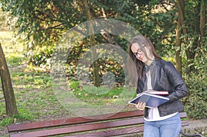 Young beautiful school or college girl with glasses sitting on the bench in the park reading the books and study for exam