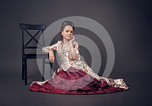 Young beautiful serious woman in medieval style dress sitting on the floor near chair