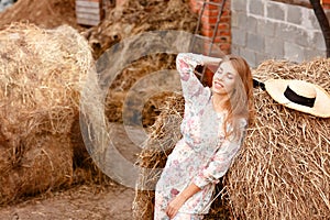 Young beautiful sexy blonde in a light dress stands next to a haystack on a summer sunny day and smiles