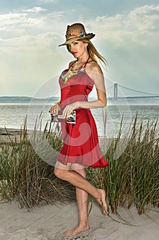 Young beautiful blonde woman wearing straw hat and elegant red dress posing on the beach.