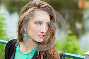 Young beautiful girl in a green dress with beautiful makeup with green shackles sitting on the river Bank in the city