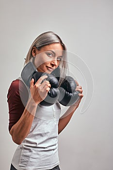 Young beautiful sexy woman boxer posing with black boxing gloves in her hands on a gray background. Copy space, gray