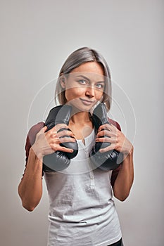 Young beautiful sexy woman boxer posing with black boxing gloves in her hands on a gray background. Copy space, gray