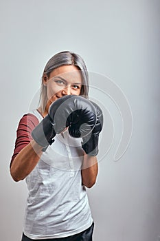 Young beautiful sexy woman boxer posing with black boxing gloves in her hands on a gray background. Copy space, gray