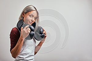 Young beautiful sexy woman boxer posing with black boxing gloves in her hands on a gray background. Copy space, gray