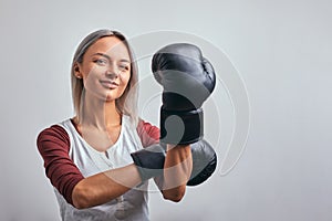 Young beautiful sexy woman boxer posing with black boxing gloves in her hands on a gray background. Copy space, gray