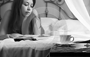 Young beautiful woman reading book on a bed in hotel room. black and white