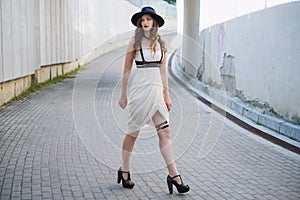 Young beautiful woman wearing trendy outfit, white dress, black hat and leather swordbelt. Longhaired brunette