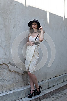 Young beautiful woman wearing trendy outfit, white dress, black hat and leather swordbelt. Longhaired brunette