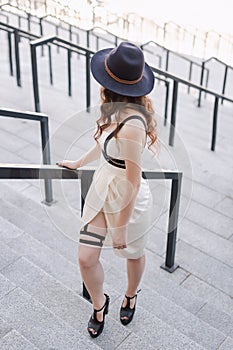 Young beautiful woman wearing trendy outfit, white dress, black hat and leather swordbelt. Longhaired brunette