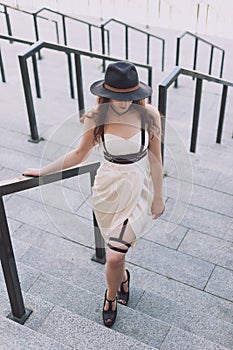 Young beautiful woman wearing trendy outfit, white dress, black hat and leather swordbelt. Longhaired brunette