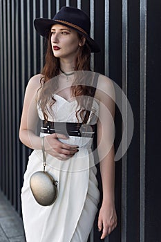 Young beautiful woman wearing trendy outfit, white dress, black hat and leather swordbelt. Longhaired brunette
