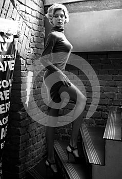 Young beautiful short hair blonde woman in black climbing the stairs, black and white photo. Side view of elegant romantic girl