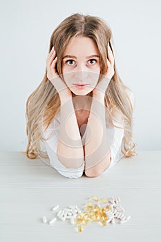 Young beautiful sick girl chooses pills, colorful capsules of tablets, vitamins, dietary supplements