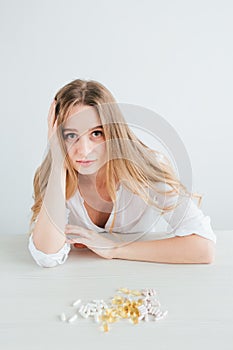 Young beautiful sick girl chooses pills, colorful capsules of tablets, vitamins, dietary supplements