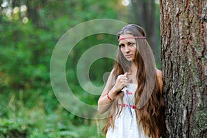 A young beautiful Slavic girl with long hair and Slavic ethnic dress stands in a summer forest with a ritual dagger in her hands