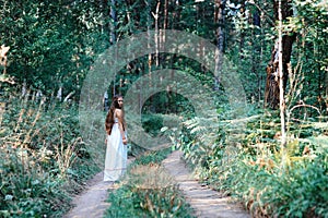 Young beautiful Slavic girl with long hair and Slavic ethnic attire walking along the trail in the summer forest