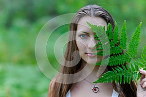 A young beautiful Slavic girl with long hair and Slavic ethnic dress covered her face with a fern leaf